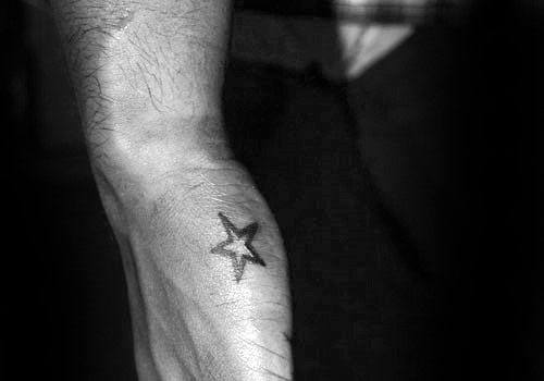 Side hand tattoo for men featuring a single bold black star placed near the edge of the hand below the pinky.