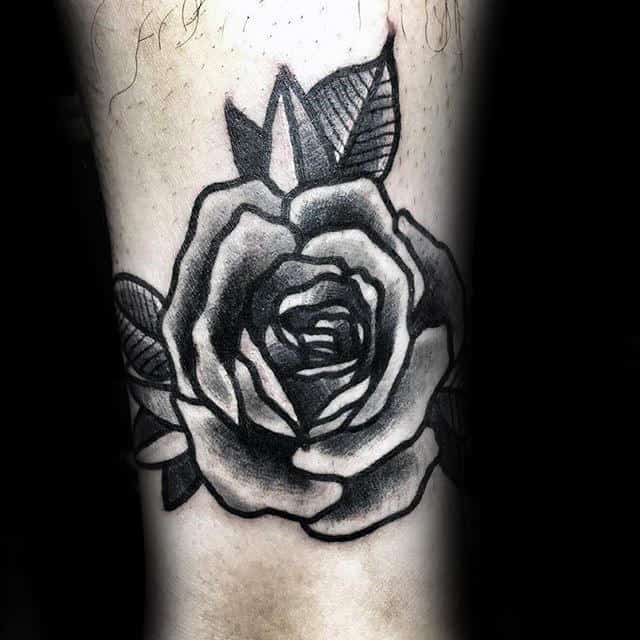 A black and grey rose tattoo with leaves on skin