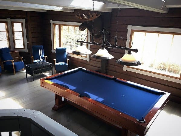 Rustic billiard room with blue felt pool table, log cabin walls, and a moose head decor piece.