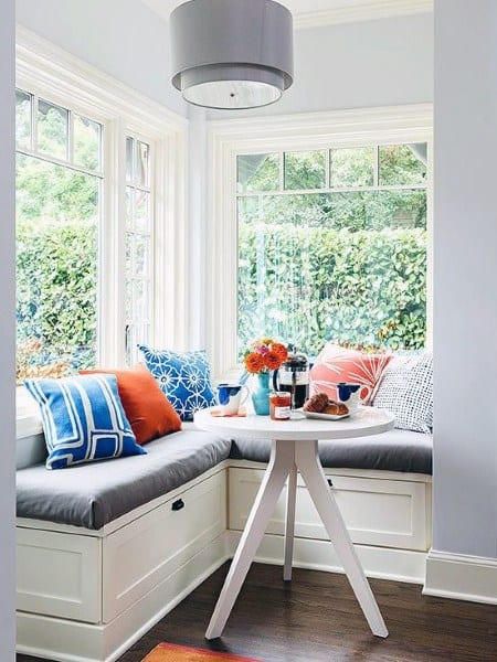 Cozy nook with a round table, colorful cushions, and large windows overlooking greenery