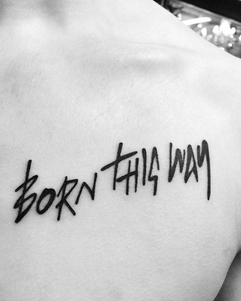 Close-up of a tattoo on skin reading "BORN THIS WAY" in bold, black script