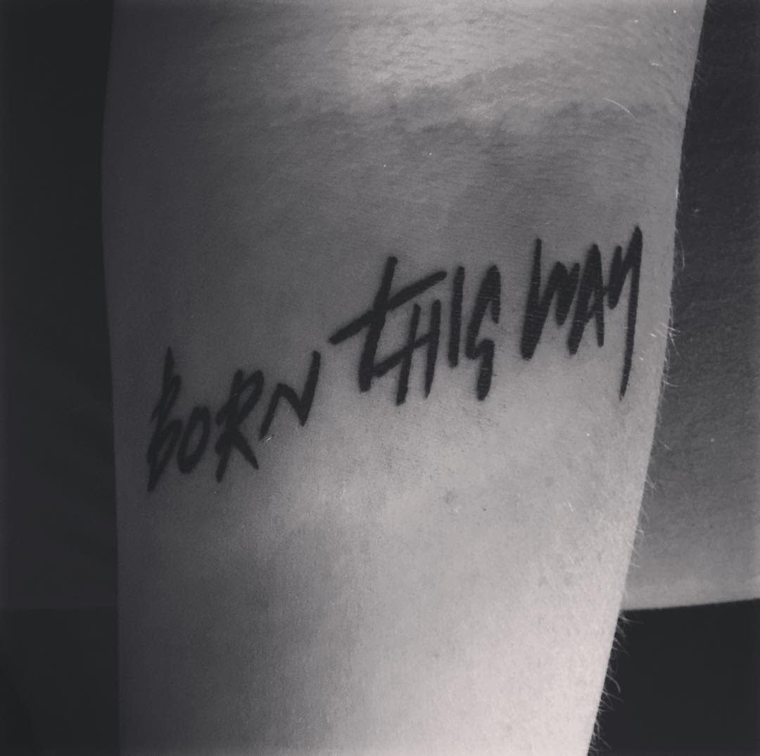 Close-up of a tattoo on skin reading "Born This Way" in black script
