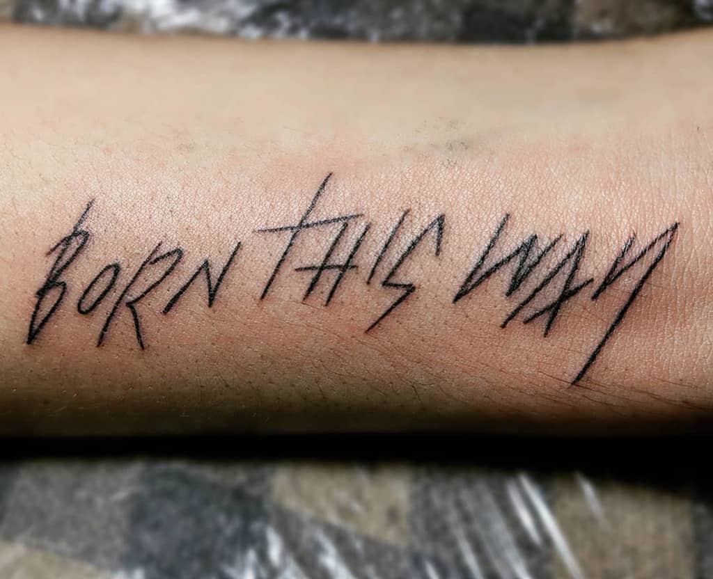 Tattoo on an arm reading "BORN THIS WAY" in bold, jagged letters