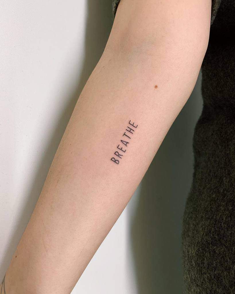 Forearm tattoo featuring the word "BREATHE" elegantly inked in a minimalist black font