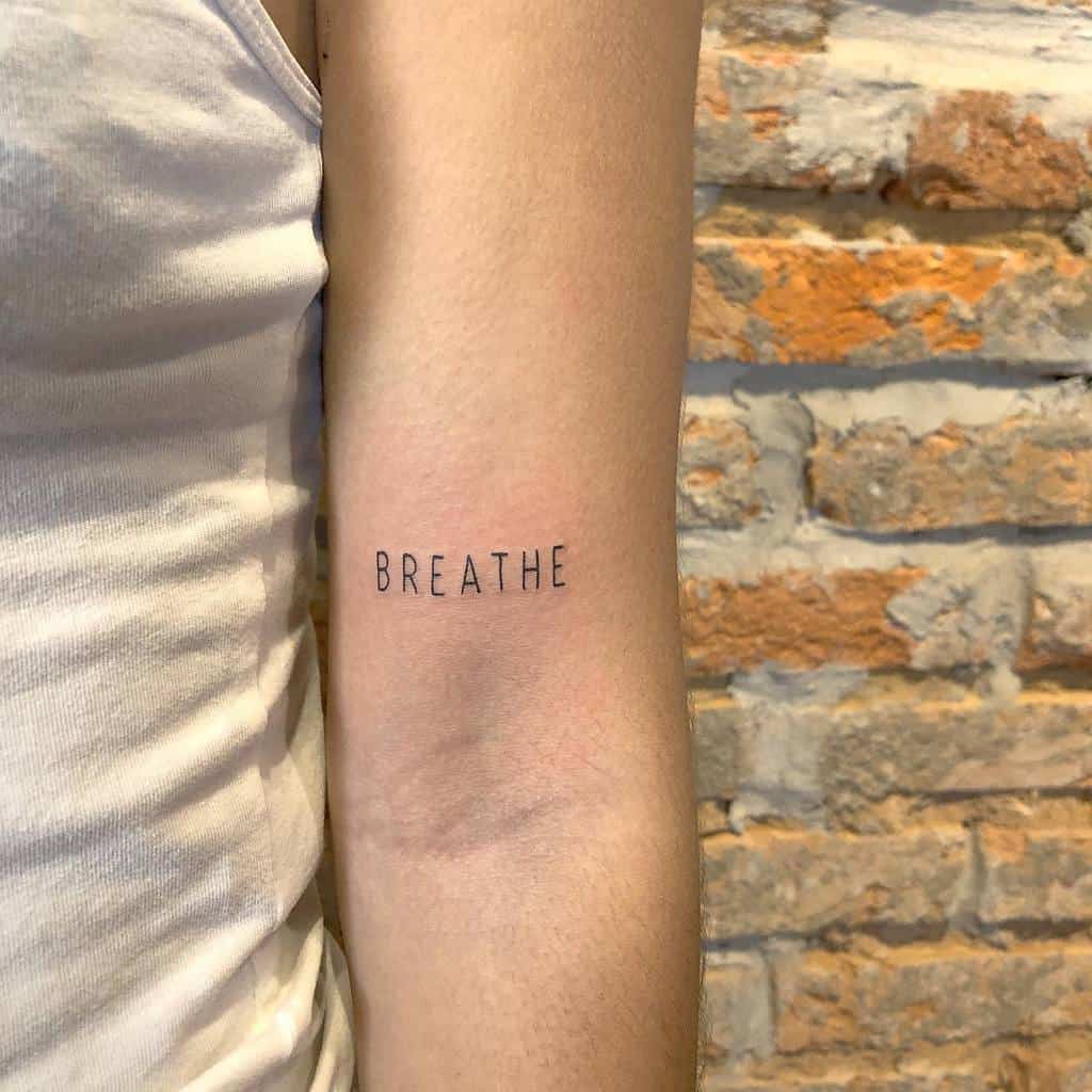 A tattoo elegantly displays the word "BREATHE" on an arm