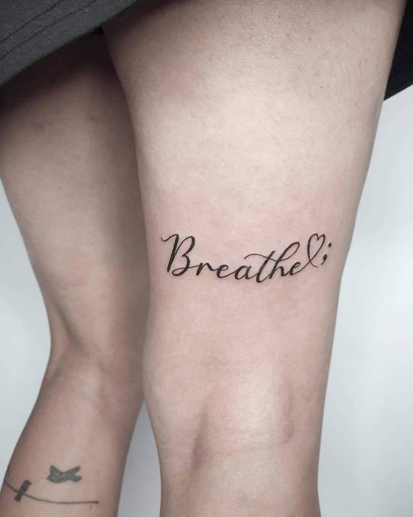 A graceful leg tattoo featuring the word "Breathe" elegantly scripted alongside a delicate heart