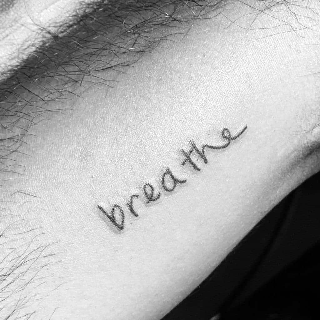 A close-up showcases a beautiful tattoo with the word "breathe" elegantly scripted in cursive on the skin, capturing its essence