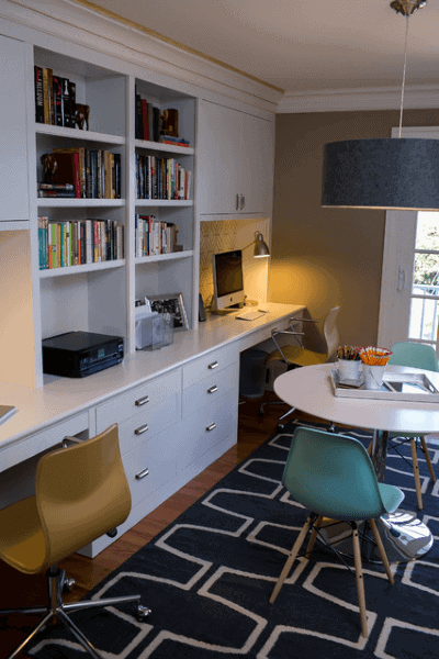 Home office with modern furniture, built-in desk, bookshelves, a computer, round table, and colorful chairs