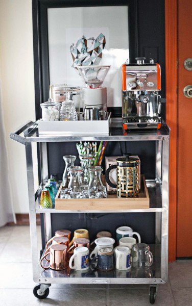 Metal coffee cart with espresso machine, glassware, mugs, and brewing accessories.