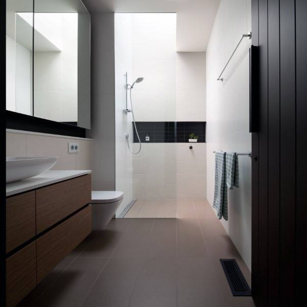 Minimalist bathroom with glass shower, wooden vanity, and natural light from skylight.