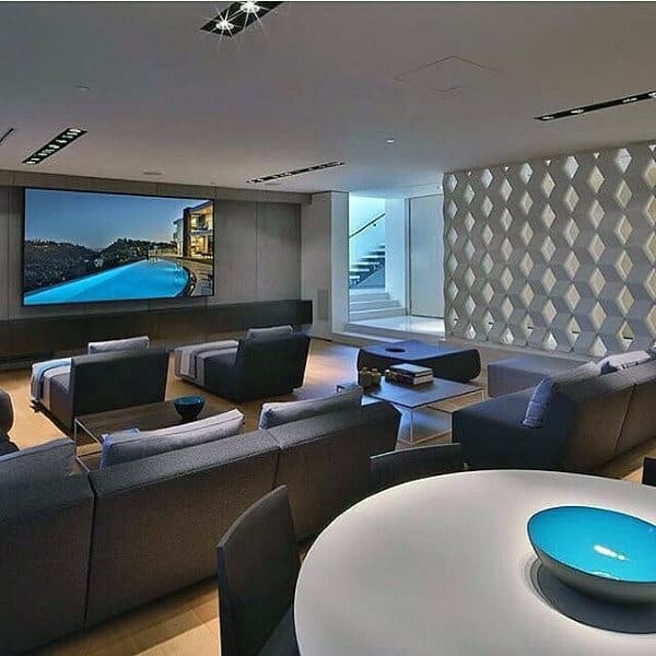 Modern home theater with plush seating, large screen, geometric wall design, and a bright blue decorative bowl