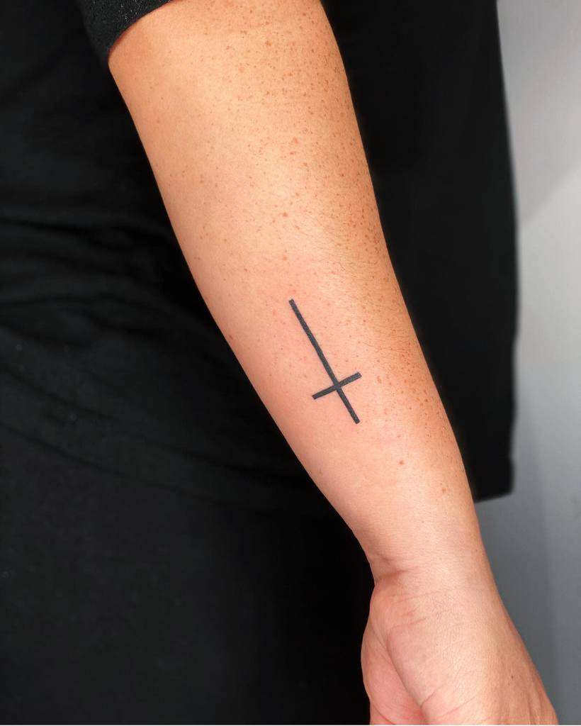 A sleek forearm displays a minimalist, inverted black cross tattoo