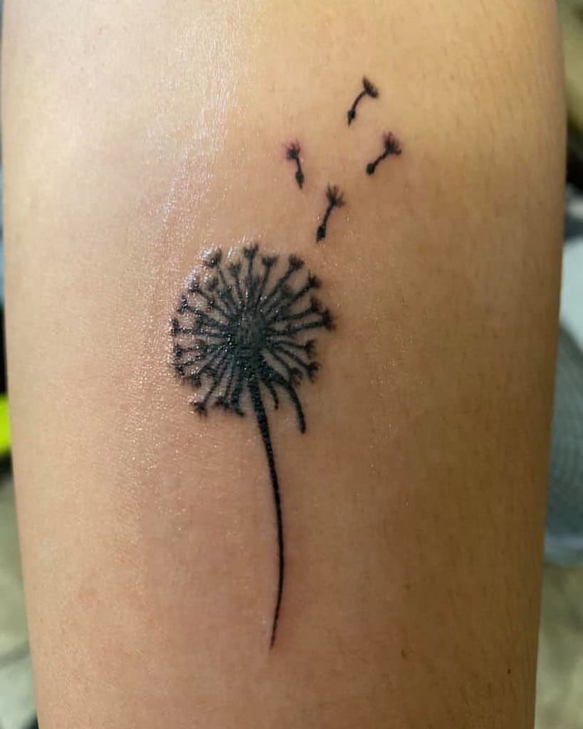 This tattoo features a simple dandelion with seeds drifting away, symbolizing the beauty of letting go and the freedom to move forward. It is elegantly placed with clean, delicate lines on the skin.