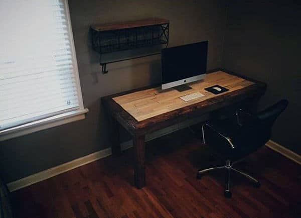 Home office with a wooden desk, computer, notebook, and leather chair on hardwood flooring near a window