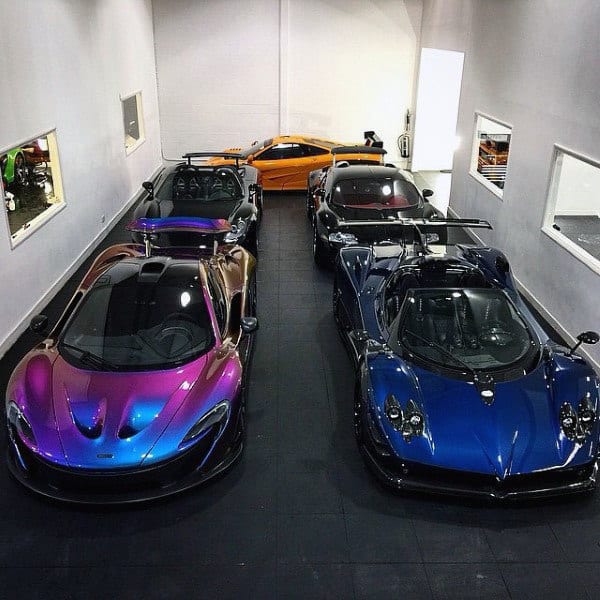 A minimalist garage showcasing a vibrant collection of luxury hypercars, including a rainbow-finish McLaren and a striking blue Pagani.