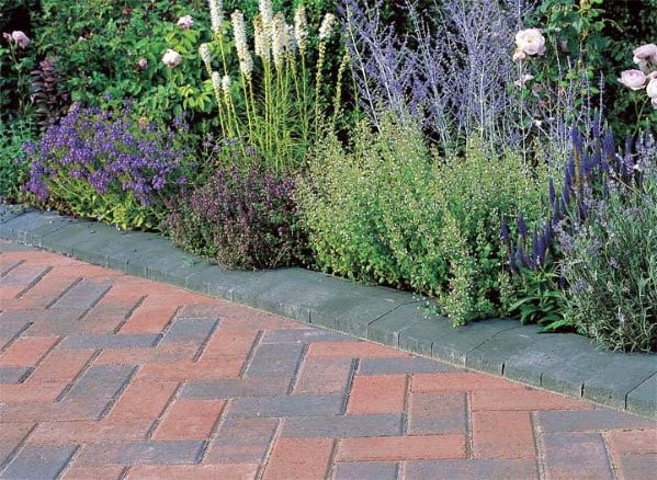 Brick-paved driveway with green stone edging and a colorful flower bed.
