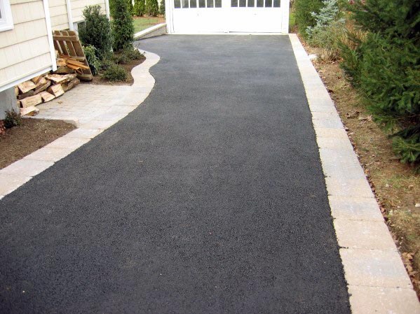 Straight asphalt driveway with brick edging leading to a white garage door.
