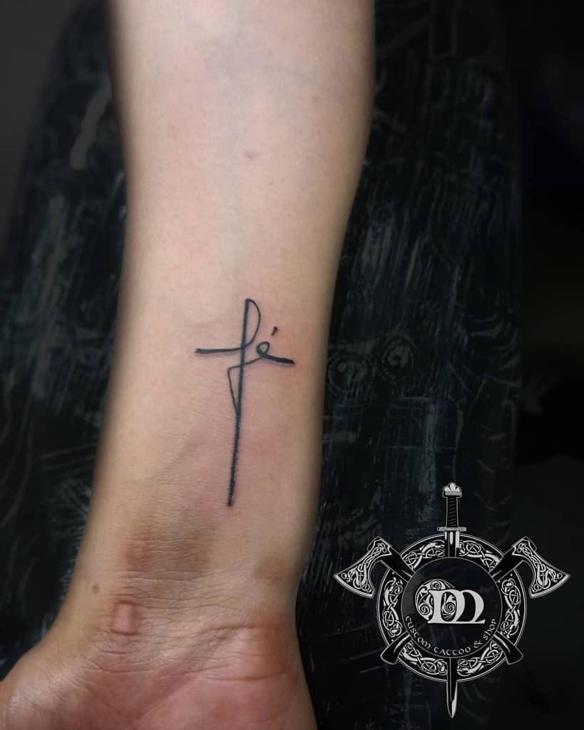 Minimalist tattoo on forearm featuring a cross intertwined with the word "fé" in cursive, symbolizing faith