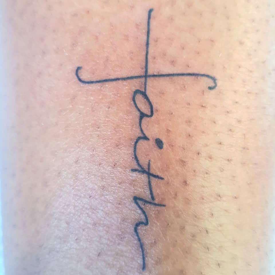 A vertical tattoo elegantly forms the word "faith," seamlessly creating the shape of a cross on the skin