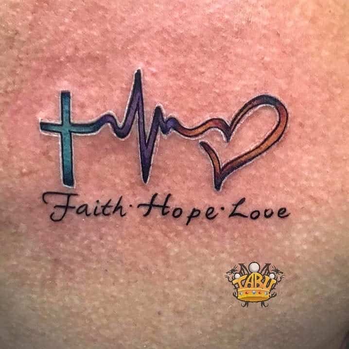 Tattoo of a cross, heartbeat line, and heart with the words "Faith Hope Love" elegantly written below