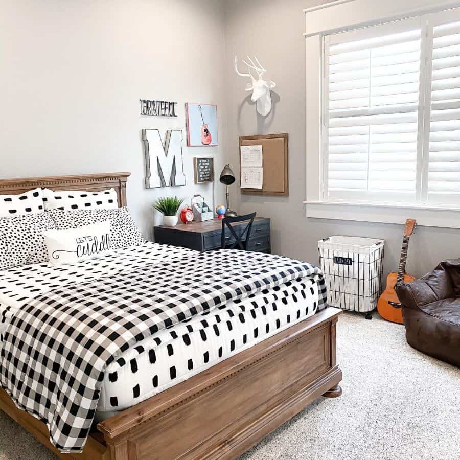 Cozy bedroom with a checkered bedspread, wall decor, desk, guitar, and bean bag chair near a window with shutters