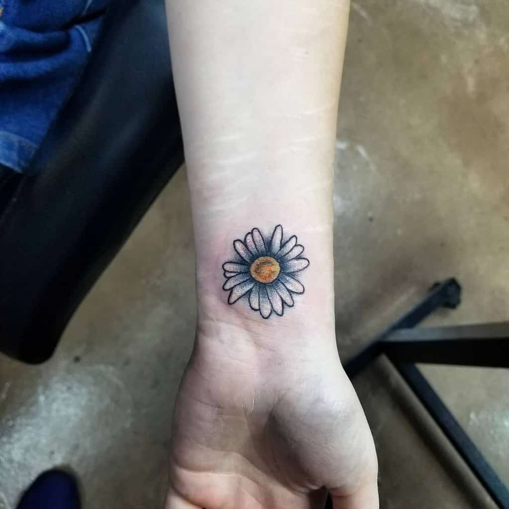 Small and simple daisy tattoo with white petals and a yellow center, placed on the inner wrist