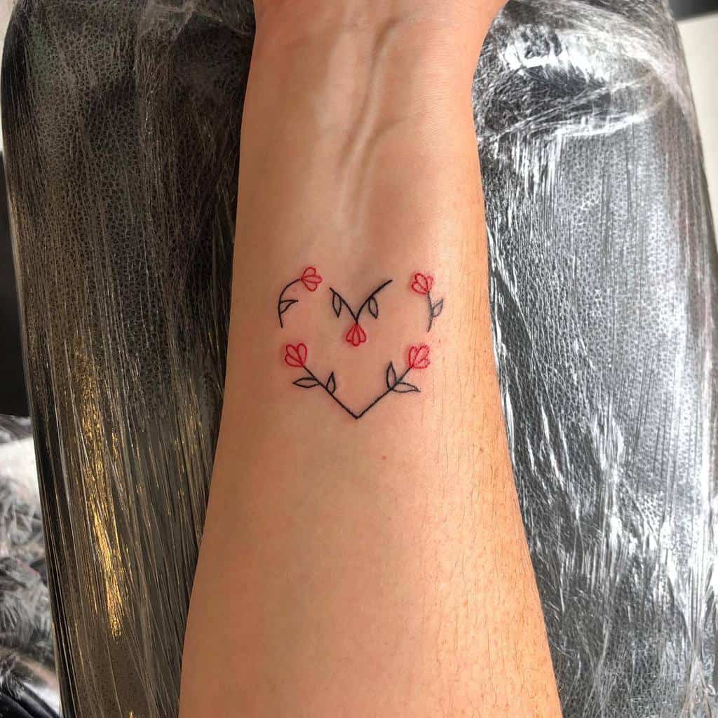 Minimalist heart-shaped tattoo formed by small flowers and stems, with delicate red petals, placed on the inner wrist
