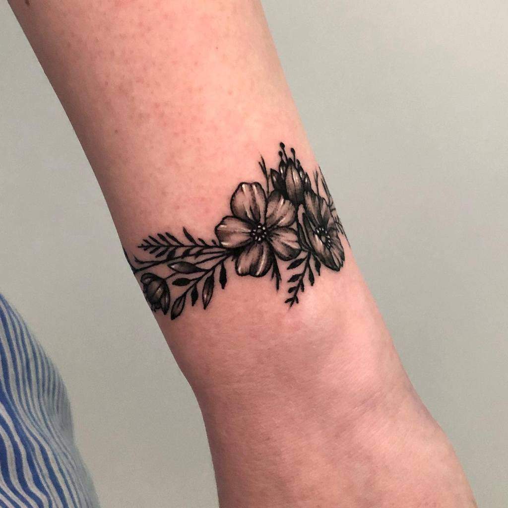 Forearm tattoo of black and white flowers and leaves gracefully extends towards the wrist, beautifully accentuating the person’s