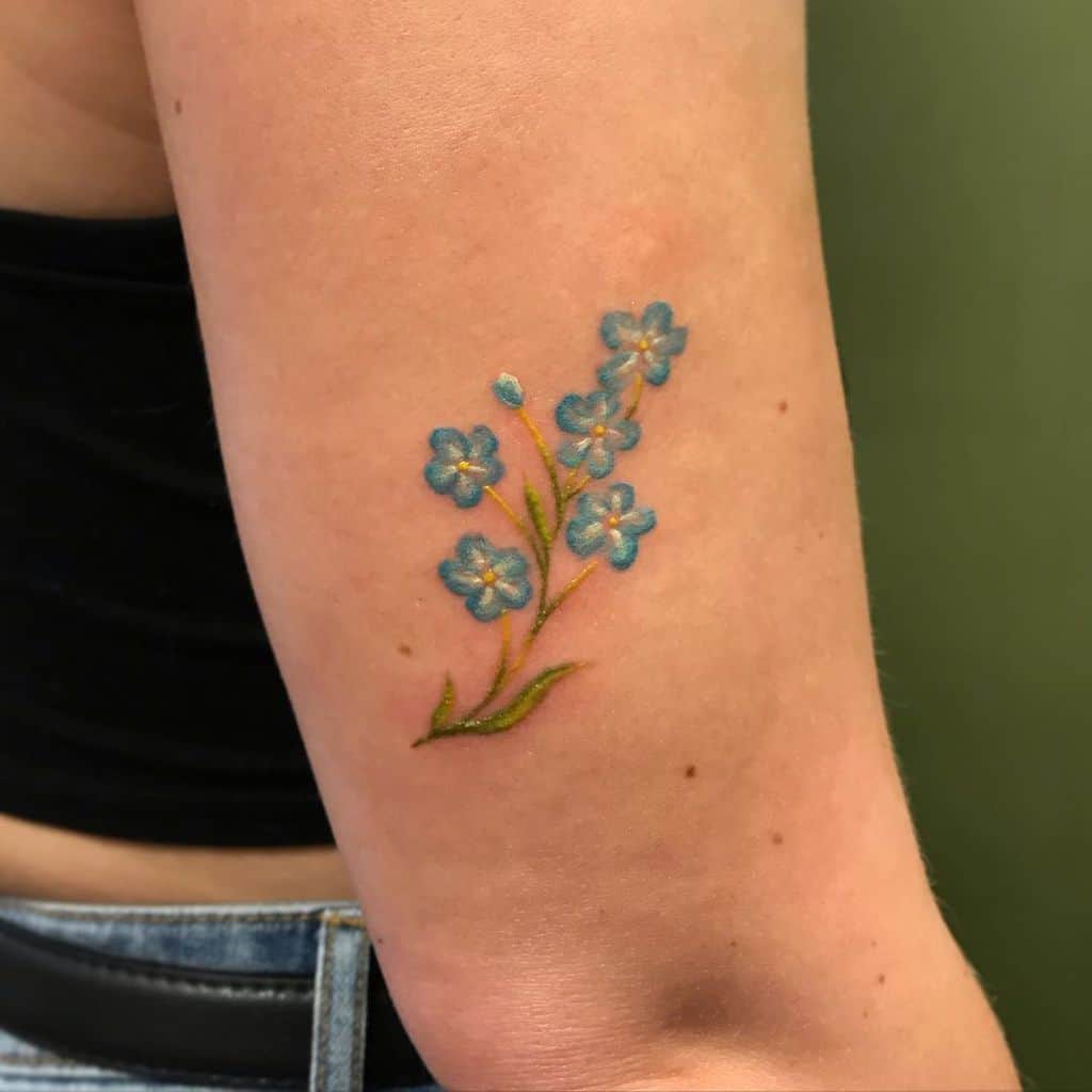 Tattoo of blue forget-me-not flowers with green stems elegantly winding along an arm