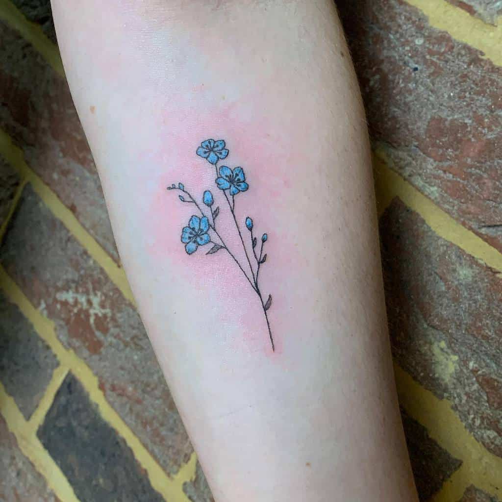A minimalistic tattoo of a delicate forget-me-not flower cluster with soft blue petals and fine black ink outlines, placed on the forearm