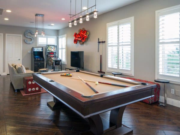 Game room with a pool table, arcade machines, TV, and seating area featuring wood flooring and bright windows