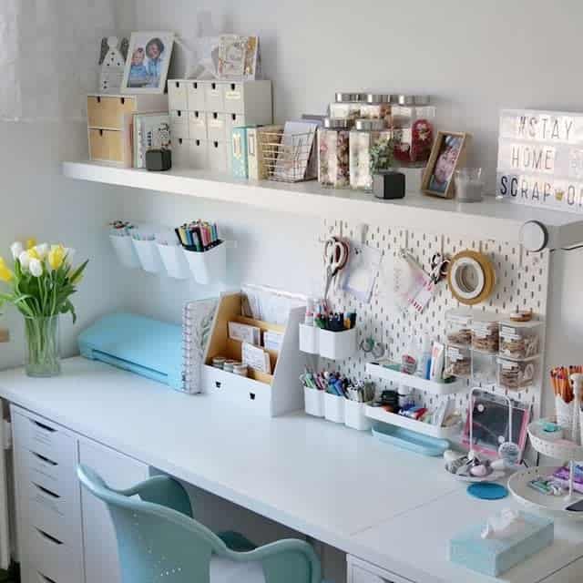A tidy, well-organized craft desk with supplies, storage bins, and decorative touches, including flowers and photos