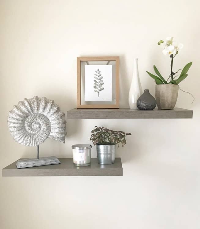 Simple grey floating shelves with potted plants, decorative vase, framed artwork, and candle.