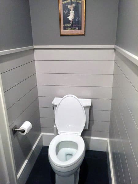 A small half bath with a white toilet, gray walls, white paneling, and a vintage poster on the wall