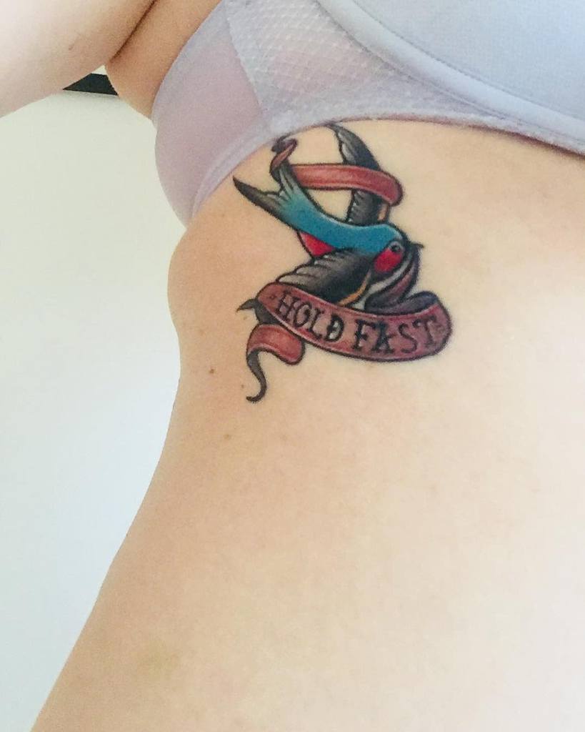 Tattoo of a bird with a "Hold Fast" banner on a woman's side
