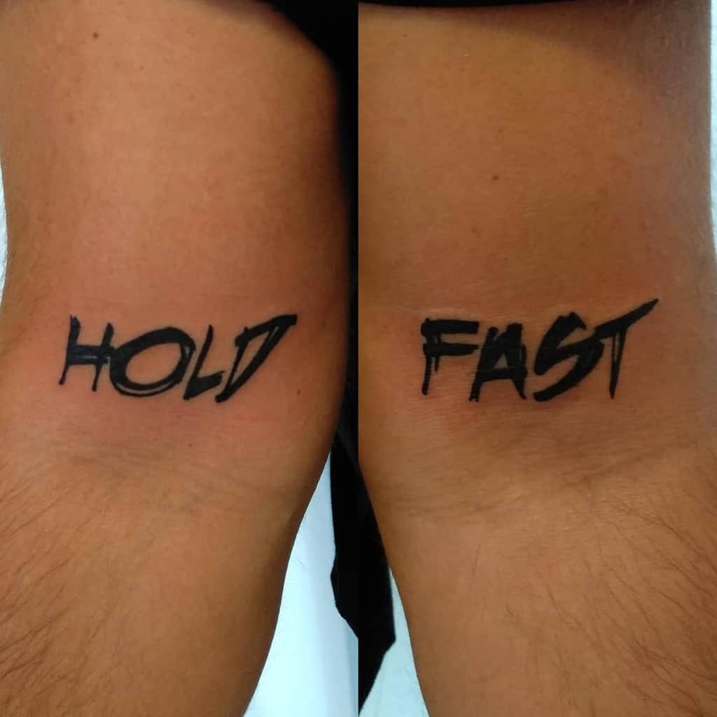 Tattoos on inner arms reading "HOLD" and "FAST" in bold black letters