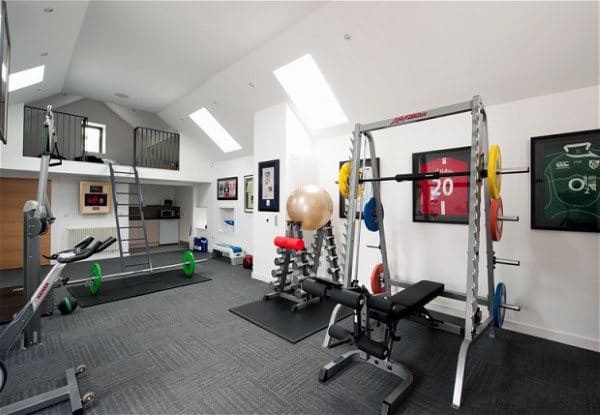 Home gym with exercise equipment, framed home sports jerseys on the wall, and loft space with a ladder on the left