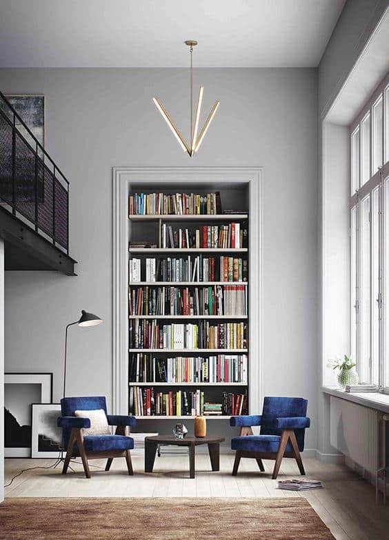 Modern living room with a floor-to-ceiling bookshelf, two blue chairs, a coffee table, and a geometric pendant light
