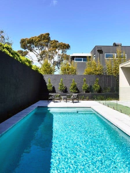 Modern backyard with a blue swimming pool, black wall, and two chairs on a sunny day