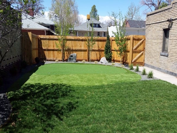 Simple backyard with a small putting green, wooden privacy fence, and landscaped greenery.
