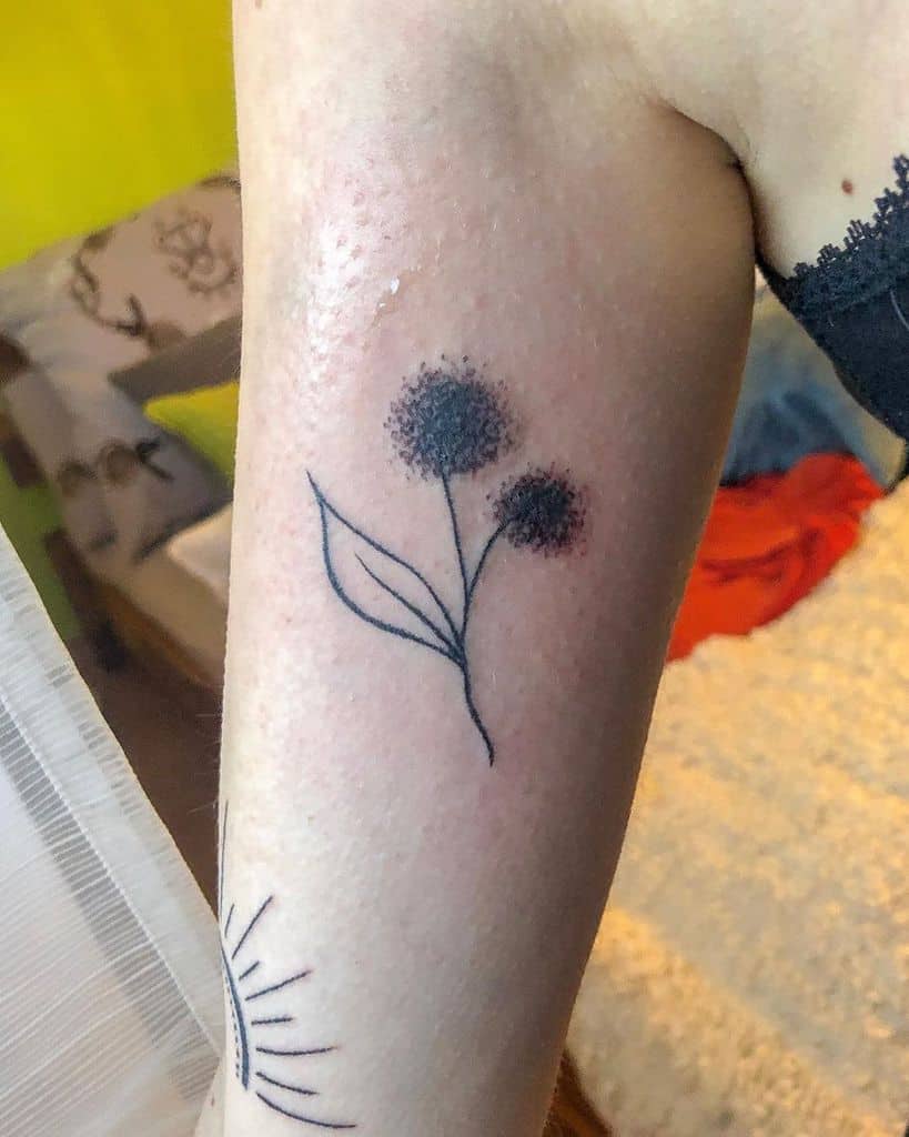 Minimalist dandelion tattoo on the upper arm with soft dot shading, symbolizing simplicity, growth, and fleeting beauty.