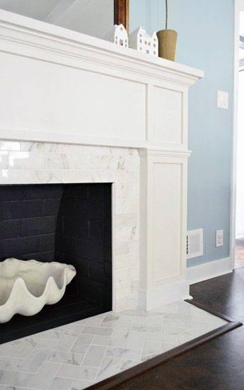 White marble fireplace with a classic white wood mantel and a herringbone-patterned hearth.