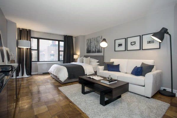 Spacious studio with cozy bed, white sofa, wooden floors, and modern decor accents.