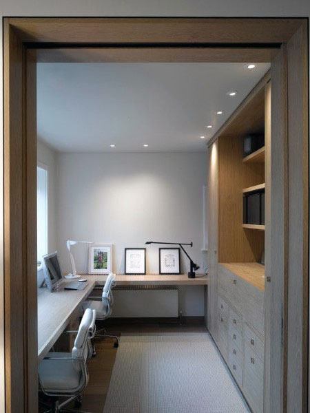 Compact home office with built-in wooden shelves, white chairs, and minimalist decor.