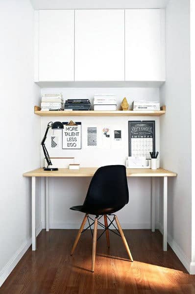 Minimalist workspace with a wooden desk, black chair, desk lamp, wall art, shelves, and books