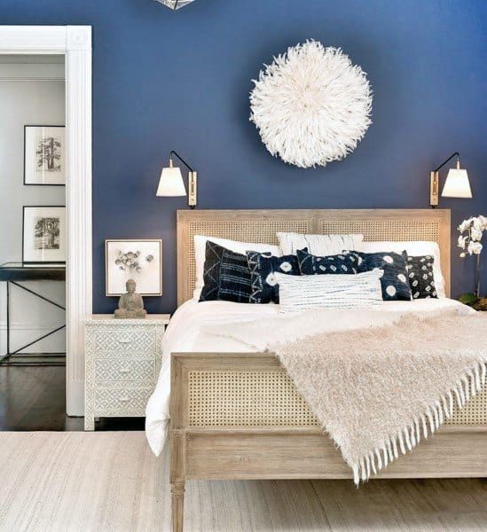 Navy bedroom with rattan bed frame, white accents, and decorative wall art.