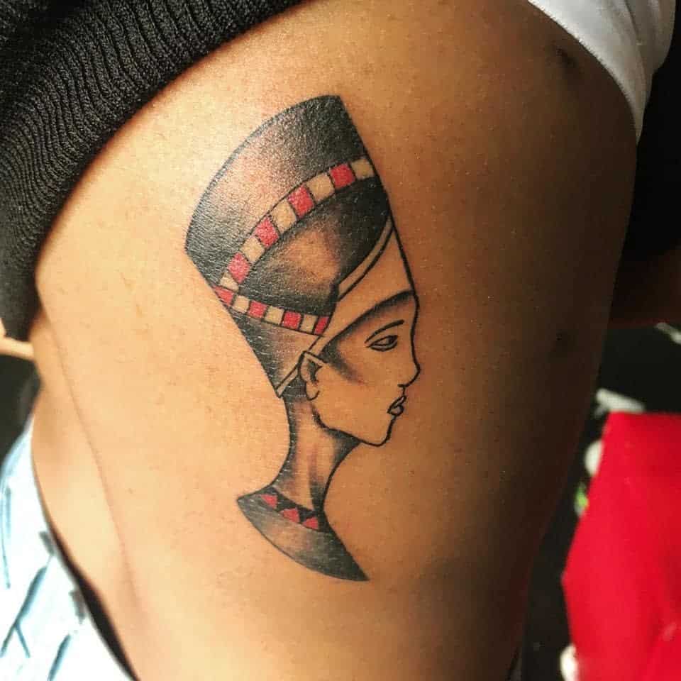 Tattoo of an Egyptian queen's profile in black and red ink on a side torso