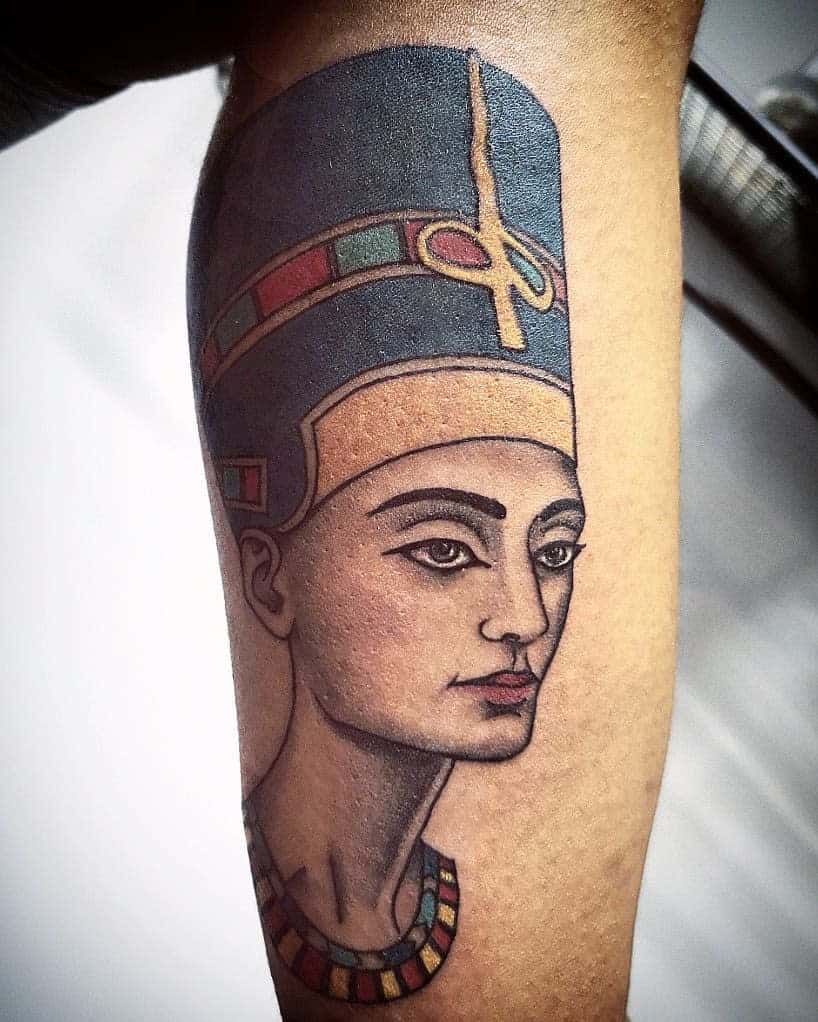 Tattoo of an ancient Egyptian figure with a tall headdress and colorful necklace on an arm