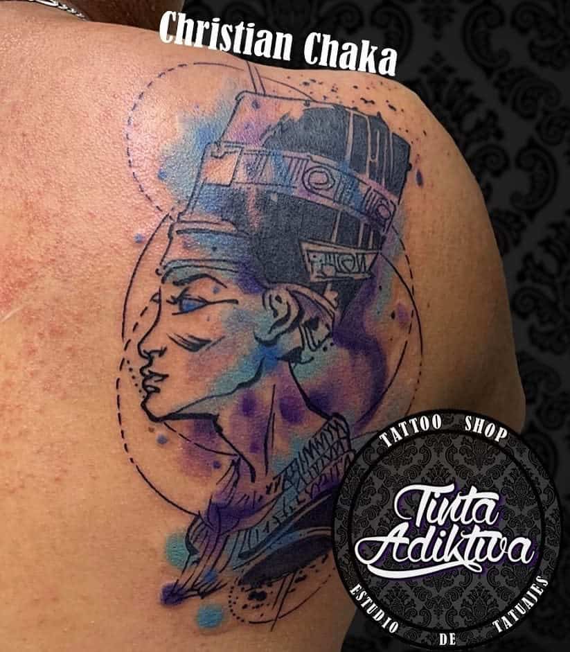 Shoulder tattoo of Queen Nefertiti with fine line art and vibrant watercolor splashes in blue and purple hues