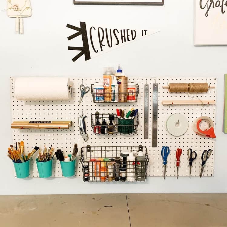 A pegboard with art supplies, scissors, paints, and storage baskets organized on a wall